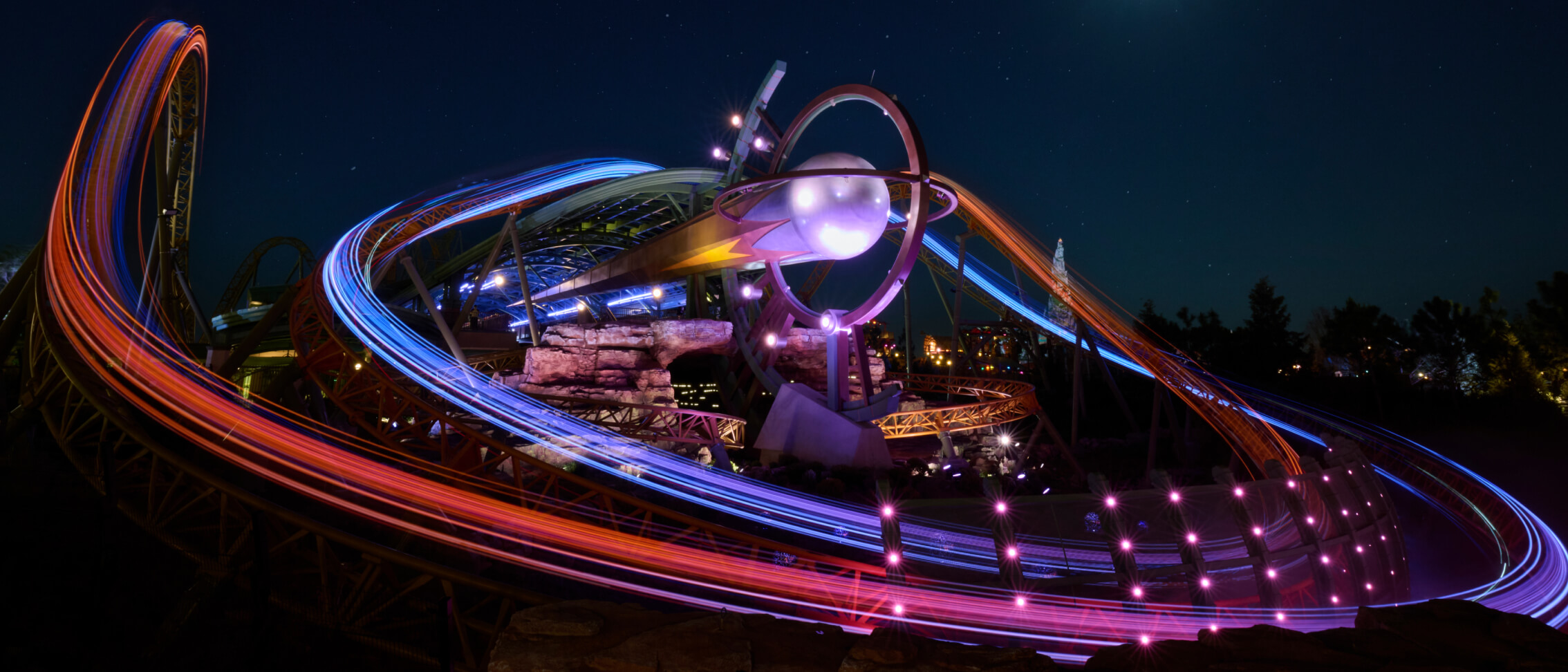 Stardust Racers roller coaster at night with illuminated coaster trains creating colorful light trails in Celestial Park at Universal Epic Universe.