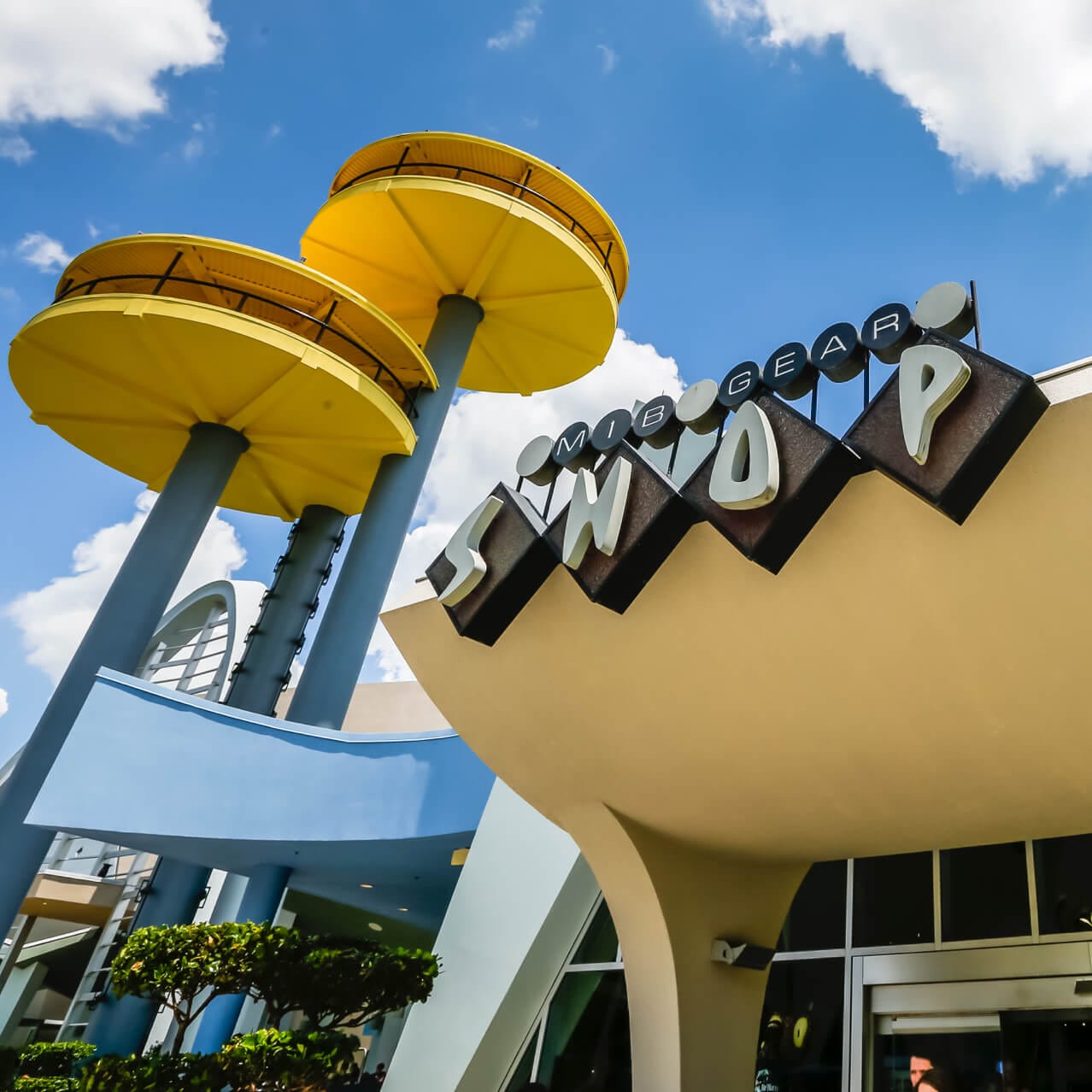 The sign for MIB Gear Shop at Universal Studios Florida, accompanied by the architectural 1964 World's Fair towers that serve as the icon for Men in Black Alien Attack.