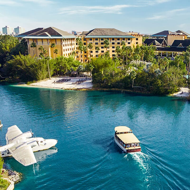 Daytime exterior photo of Loews Royal Pacific Resort overlooking the lagoon that has a boat and waterplane parked in the water.