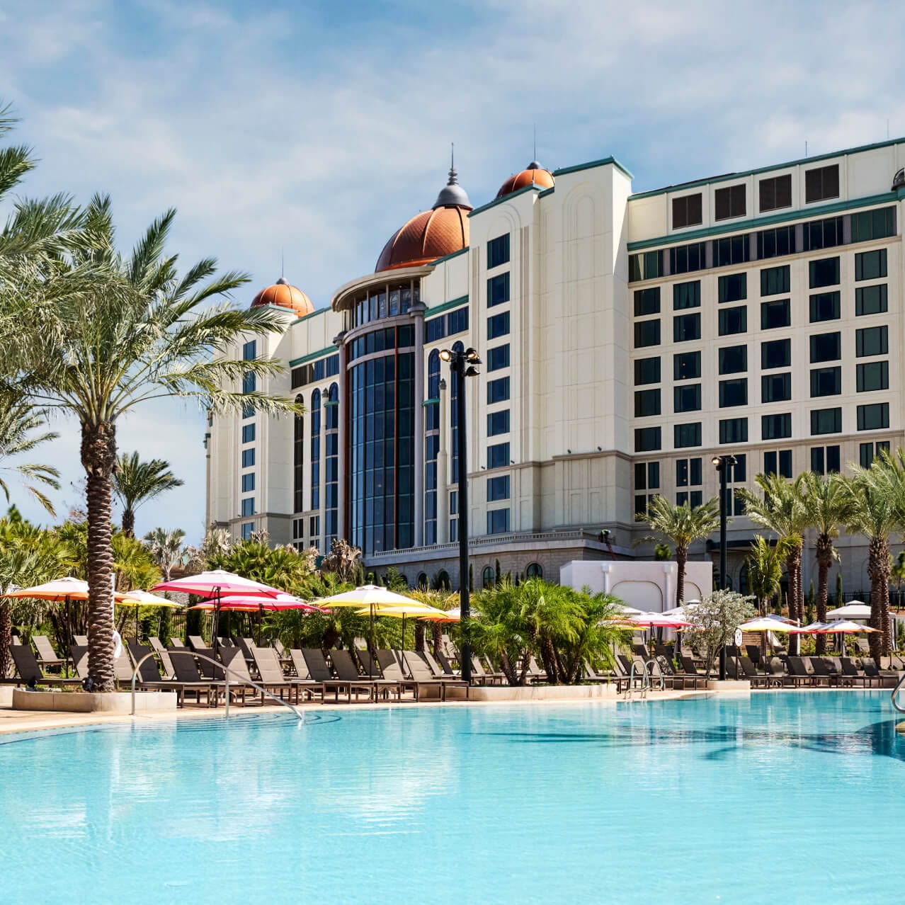 Poolside view of the Universal Helios Grand Hotel, complete with palm trees and umbrellas, at Universal Orlando Resort.