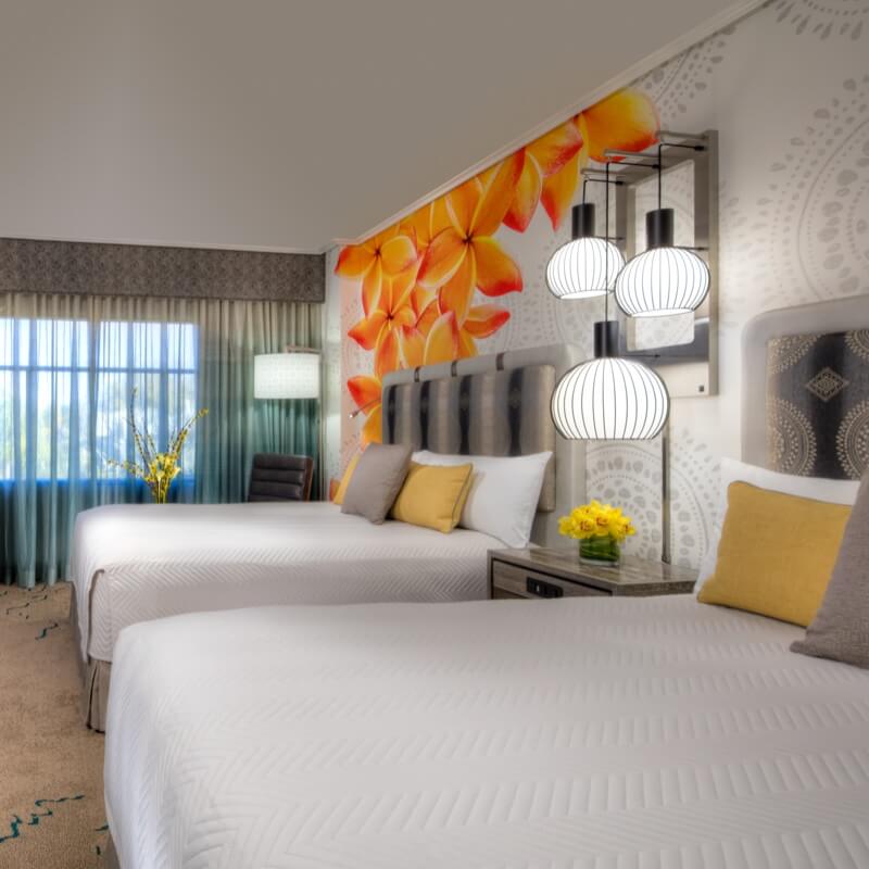 A bedroom with two beds and wallpaper with a floral design.
