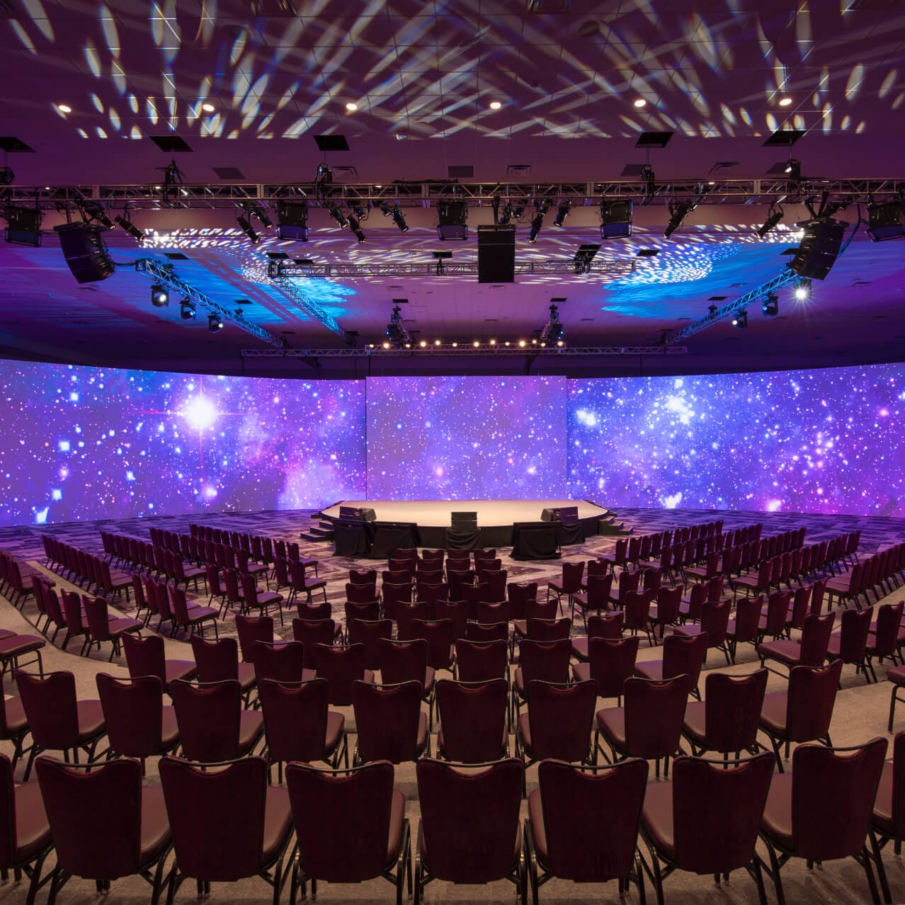 Chairs lined in rows facing a large screen in a spacious indoor meeting and event space.