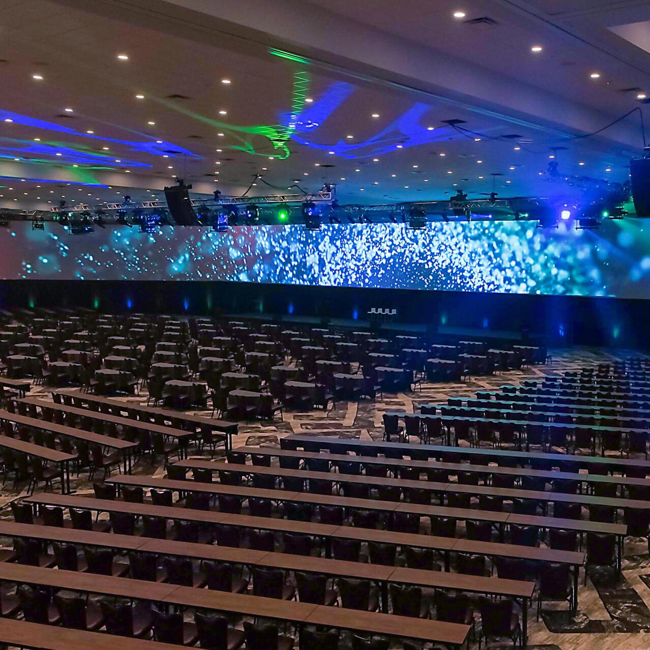 A room setup for a conference with rows of chairs and a large digital screen at the front.
