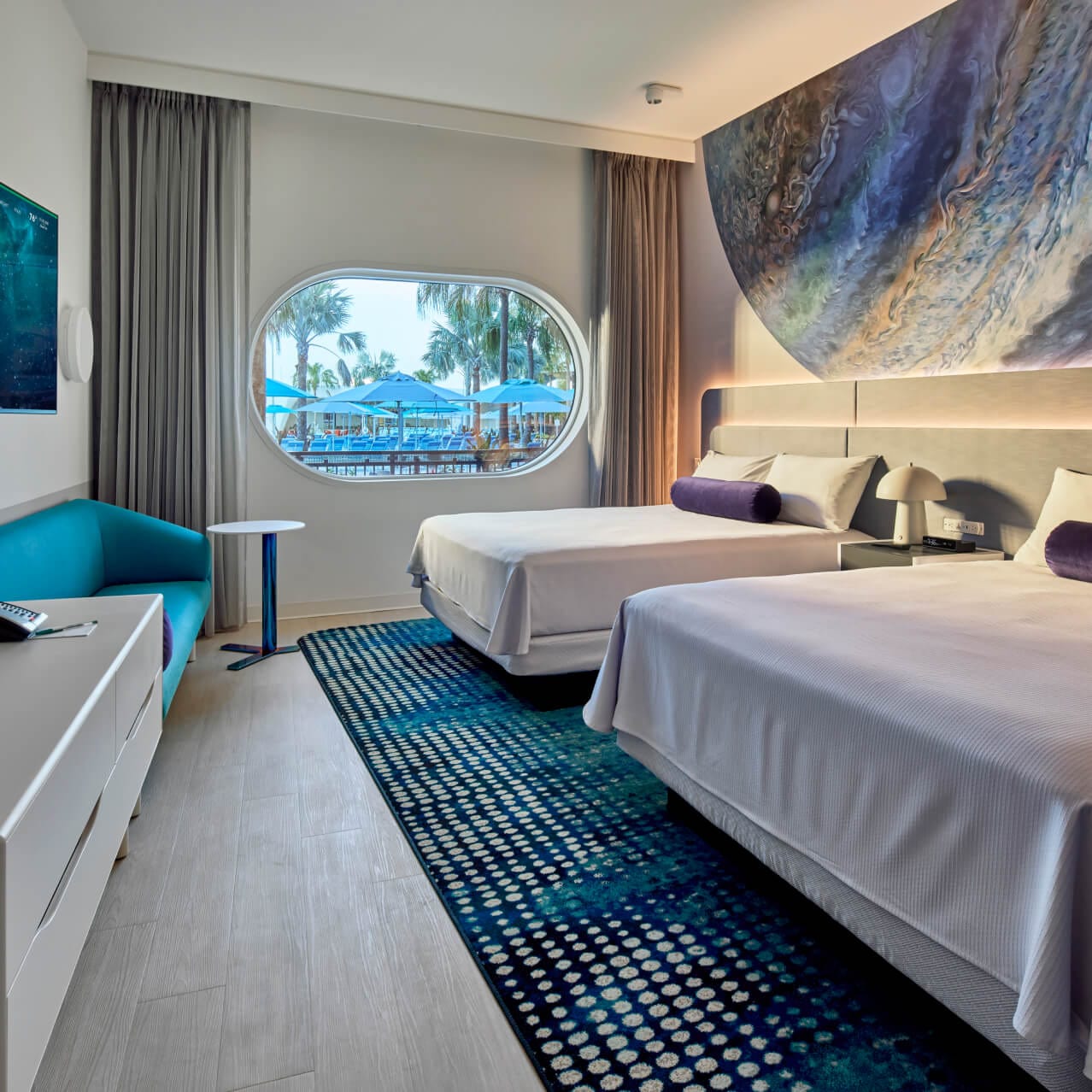 Double Queen room at Universal Terra Luna Resort, with a pool-side view out of the spaceship-styled window, galaxy-themed mural with two queen beds and flat panel TV.