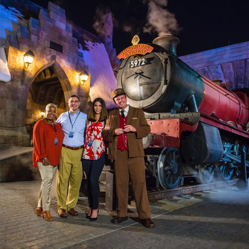 Event attendees and a conductor stand in front of the Hogwarts Express in The Wizarding World of Harry Potter Hogsmeade.
