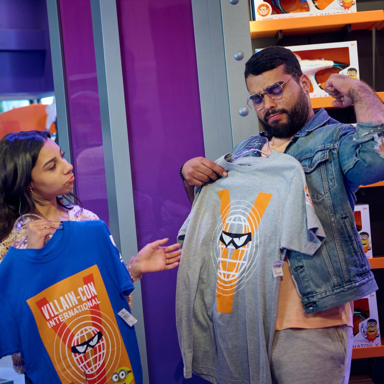 A woman and man holding Villain-Con themed t-shirts and man is posing flexing his left arm