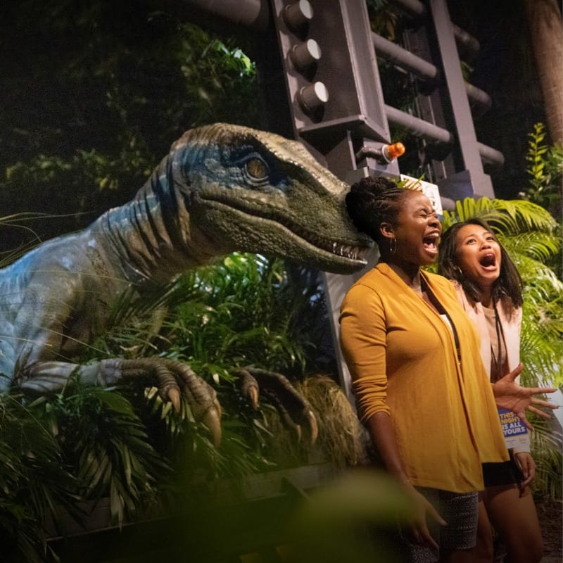 Two women screams in front of a velociraptor at Jurassic Park World