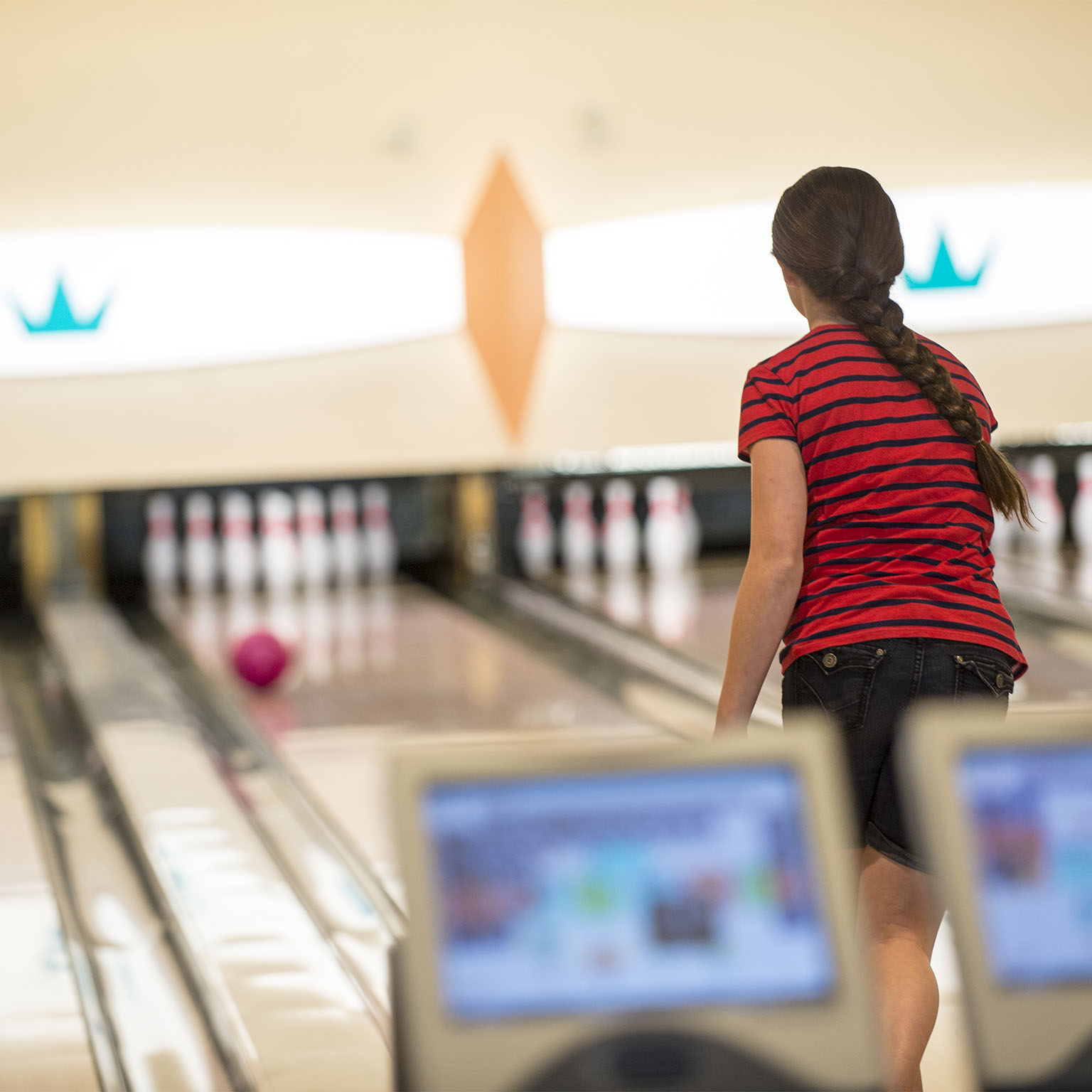 A girl in a red and black striped shirt watches as her bowling ball rolls down the lane at Universal Orlando's Galaxy Bowl.