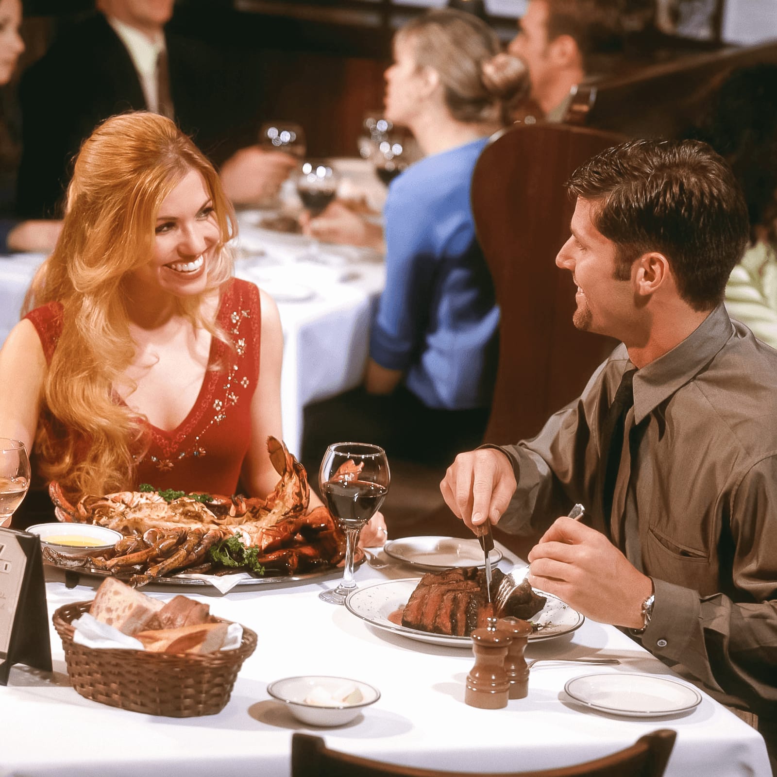 A man and woman smile over a meal of steak and seafood inside The Palm restaurant at Hard Rock Hotel at Universal Orlando.