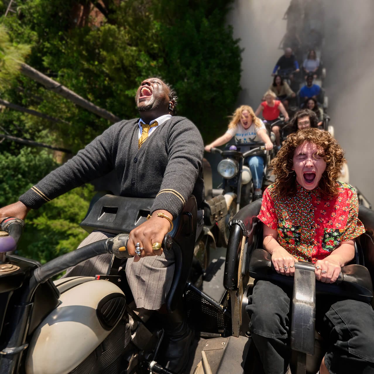 Guests screaming in delight while gripping the handlebars of their motorcycle-style vehicles as they hurtle through a forest.