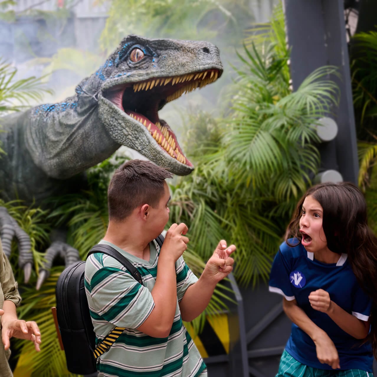 One kid making claws with his hands while another screams as Blue the Velociraptor hovers overhead with its mouth open wide.