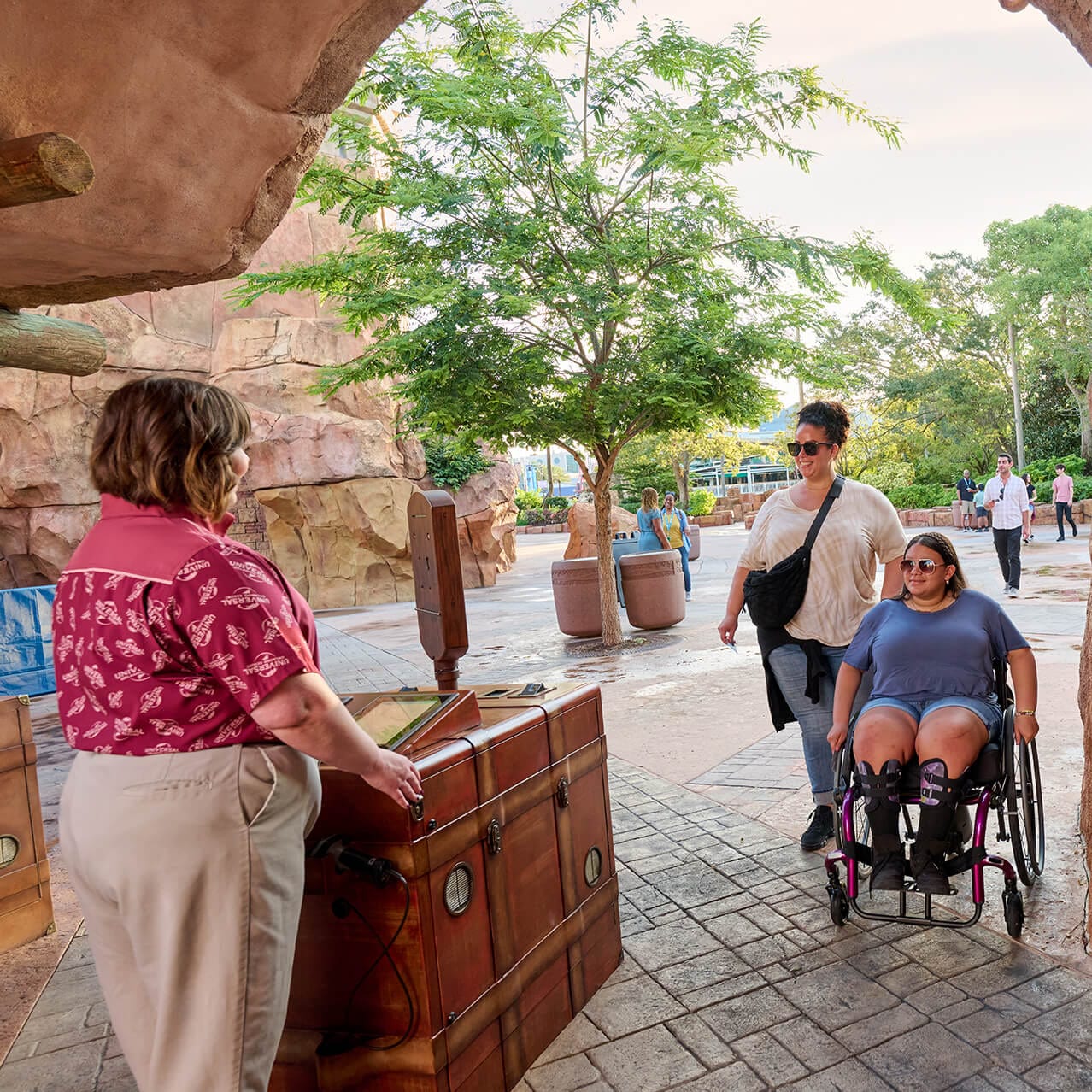A pair of friends, one using a wheelchair, approaching a Team Member stationed at the entrance of Universal Islands of Adventure.