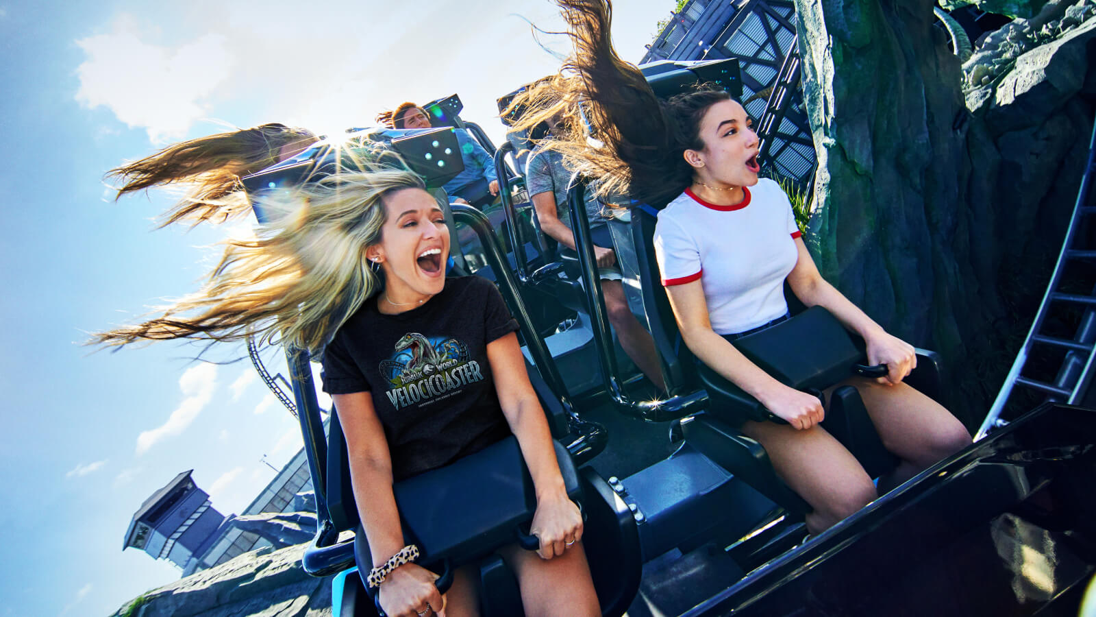 Two girls scream and smile as they grip the handles on the VelociCoaster ride at Universal Islands of Adventure.