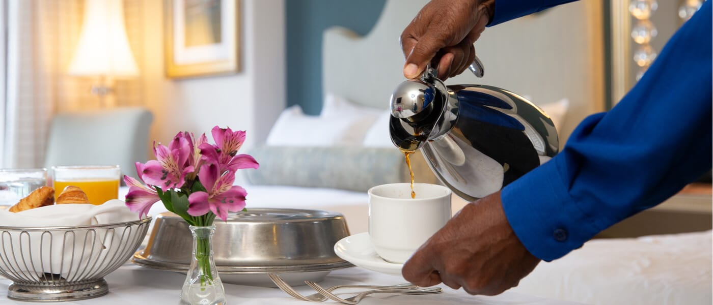 A staff member at Universal Orlando's Premier on-site resort hotel pours a cup of coffee by a table filled with room service deliveries inside a guest room at Loews Portofino Bay Hotel.