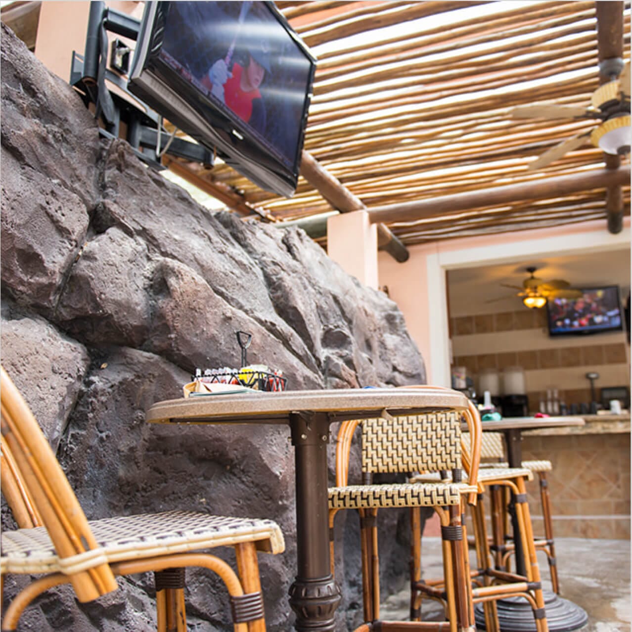 A cafe table with woven chairs beneath a flat screen TV inside the shaded dining area of Splendido Bar and Grill.