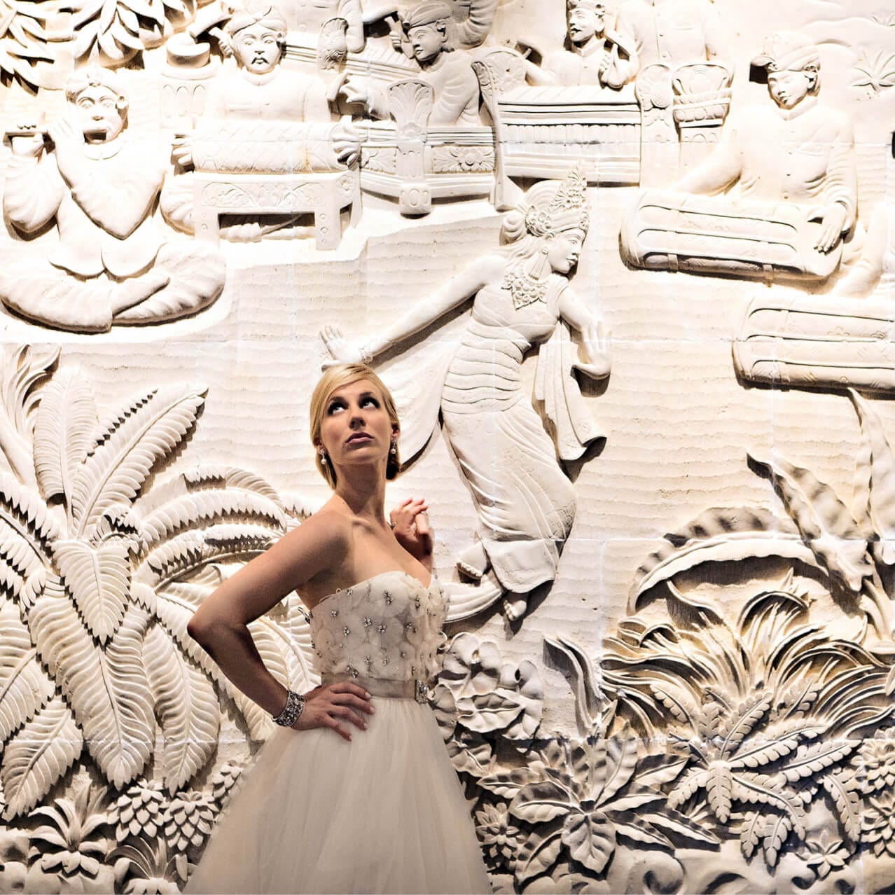 A bride poses with her hand on her hip in front of a large carved mural wall at Loews Royal Pacific Resort in Universal Orlando.