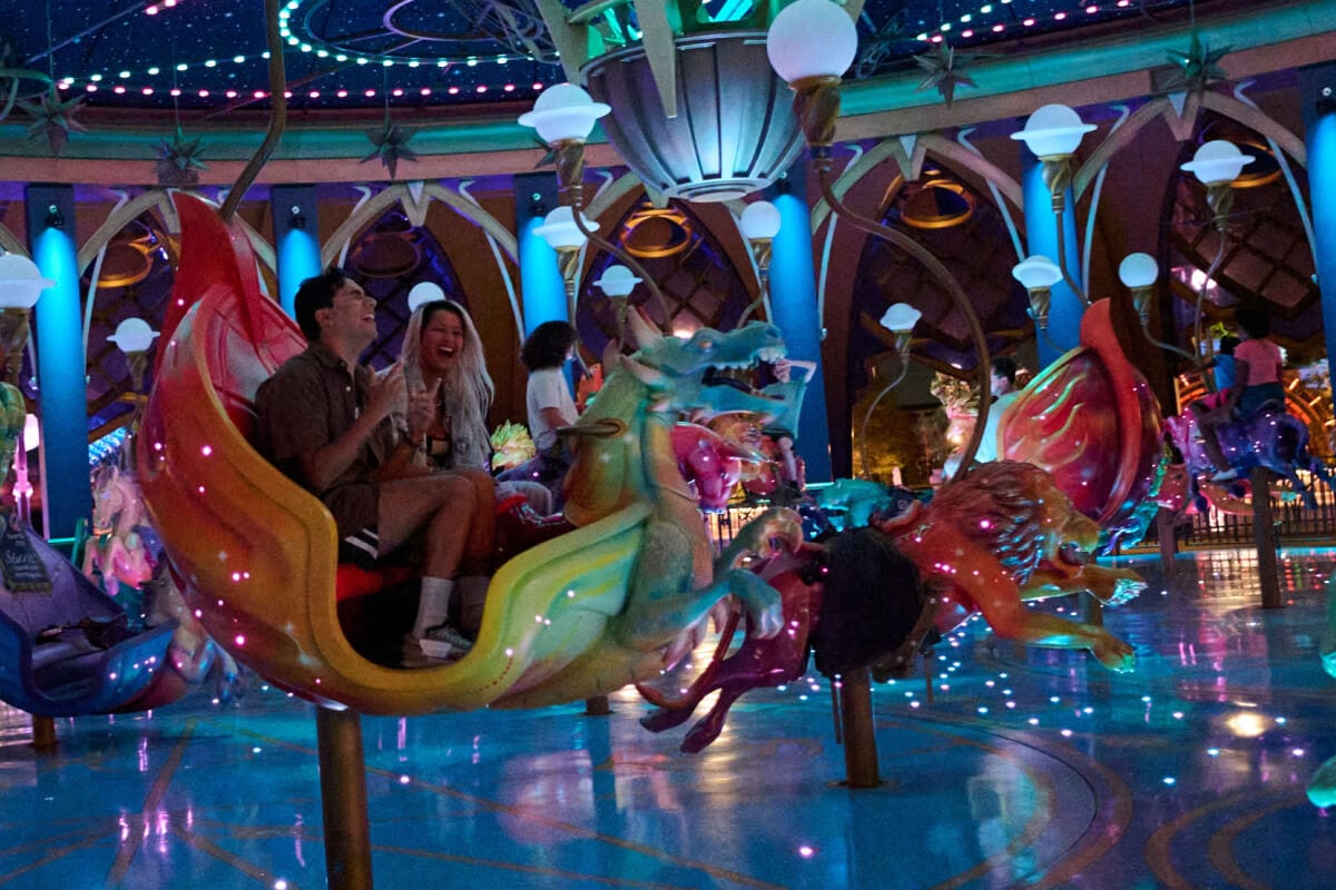 Excited Guests riding in colorful animal-shaped carousel vehicles under a ceiling of dazzling lights and starry fields.