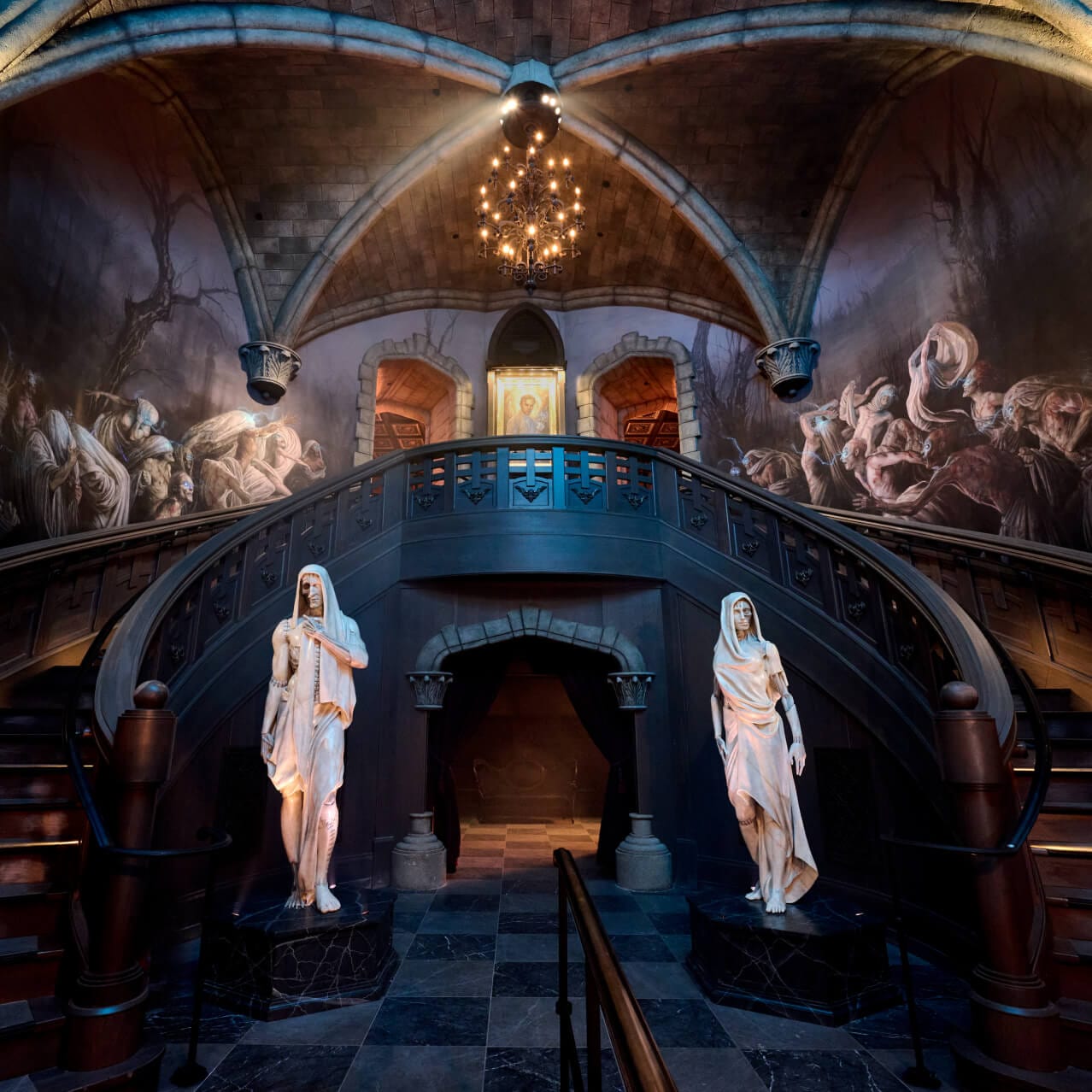 The double staircase at the entrance queue for Monsters Unchained: The Frankenstein Experiment, with marble statues and murals on the walls.