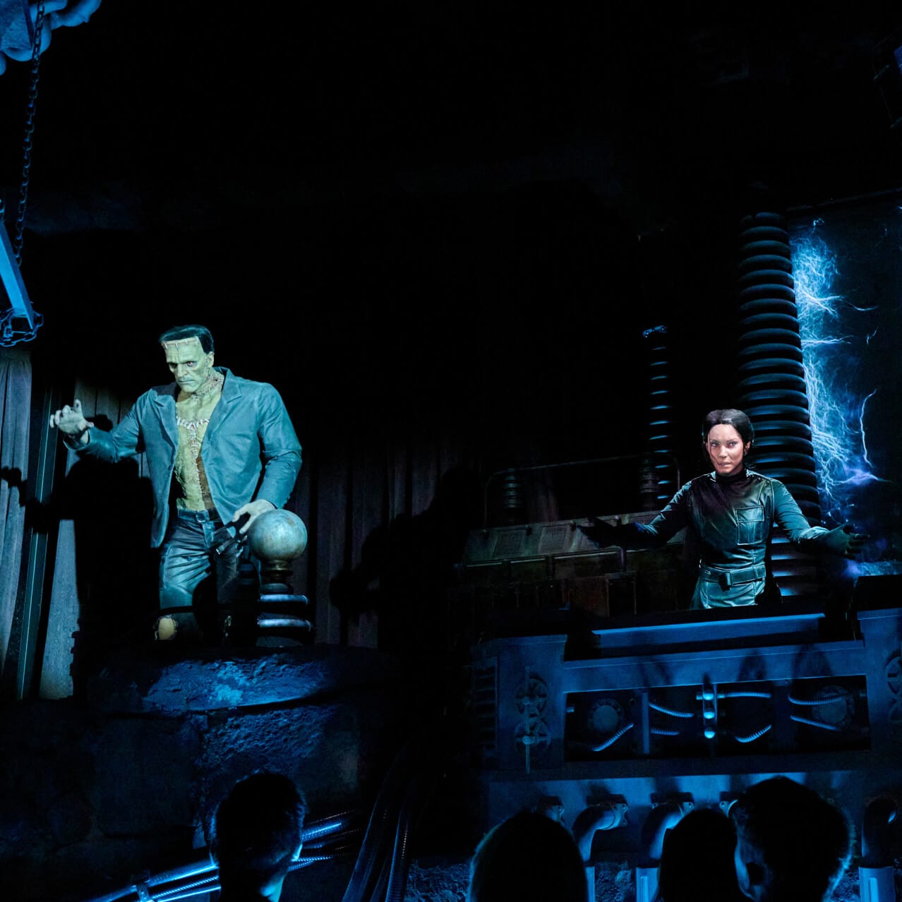 Victoria Frankenstein addresses guests while Frankenstein's Monster stands nearby on Monsters Unchained: The Frankenstein Experiment.