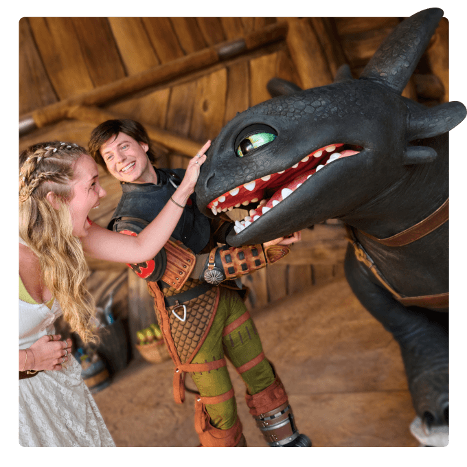 An excited Guest interacting with Toothless the dragon while a smiling Hiccup character looks.