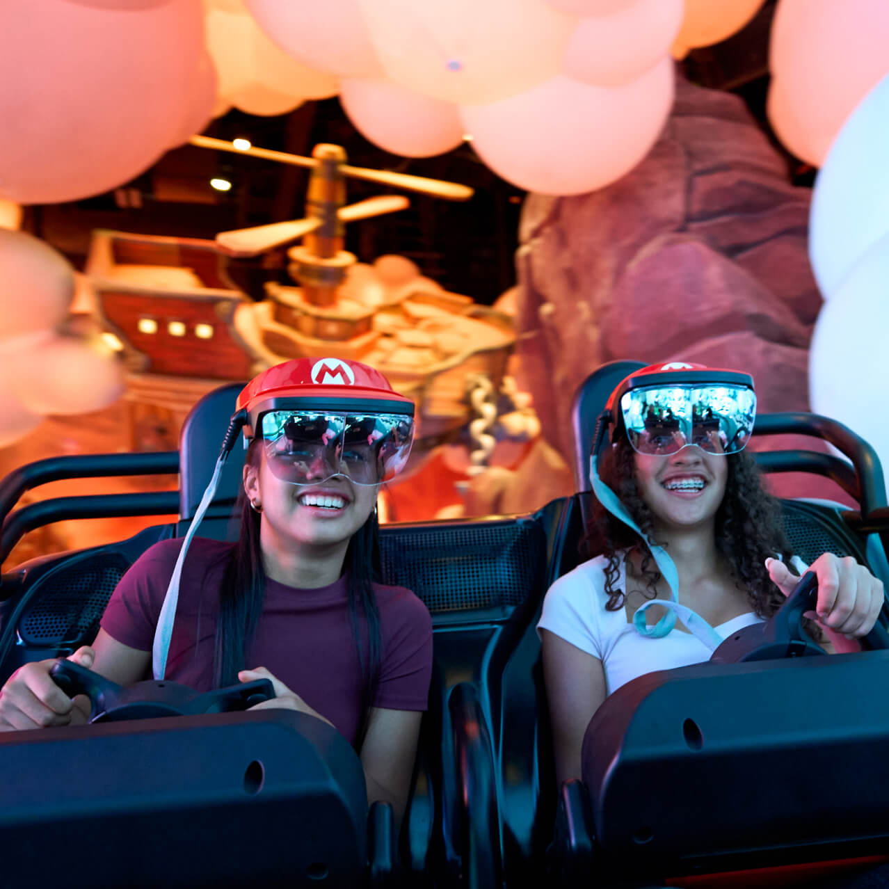 Two girls smile as they steer through Mario Kart: Bowser's Challenge in SUPER NINTENDO WORLD™ at Universal Epic Universe.