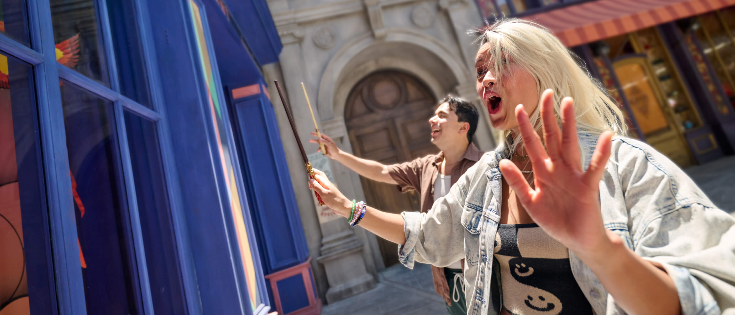 Excited Guests pointing wands at a blue storefront window on the streets of wizarding Paris.