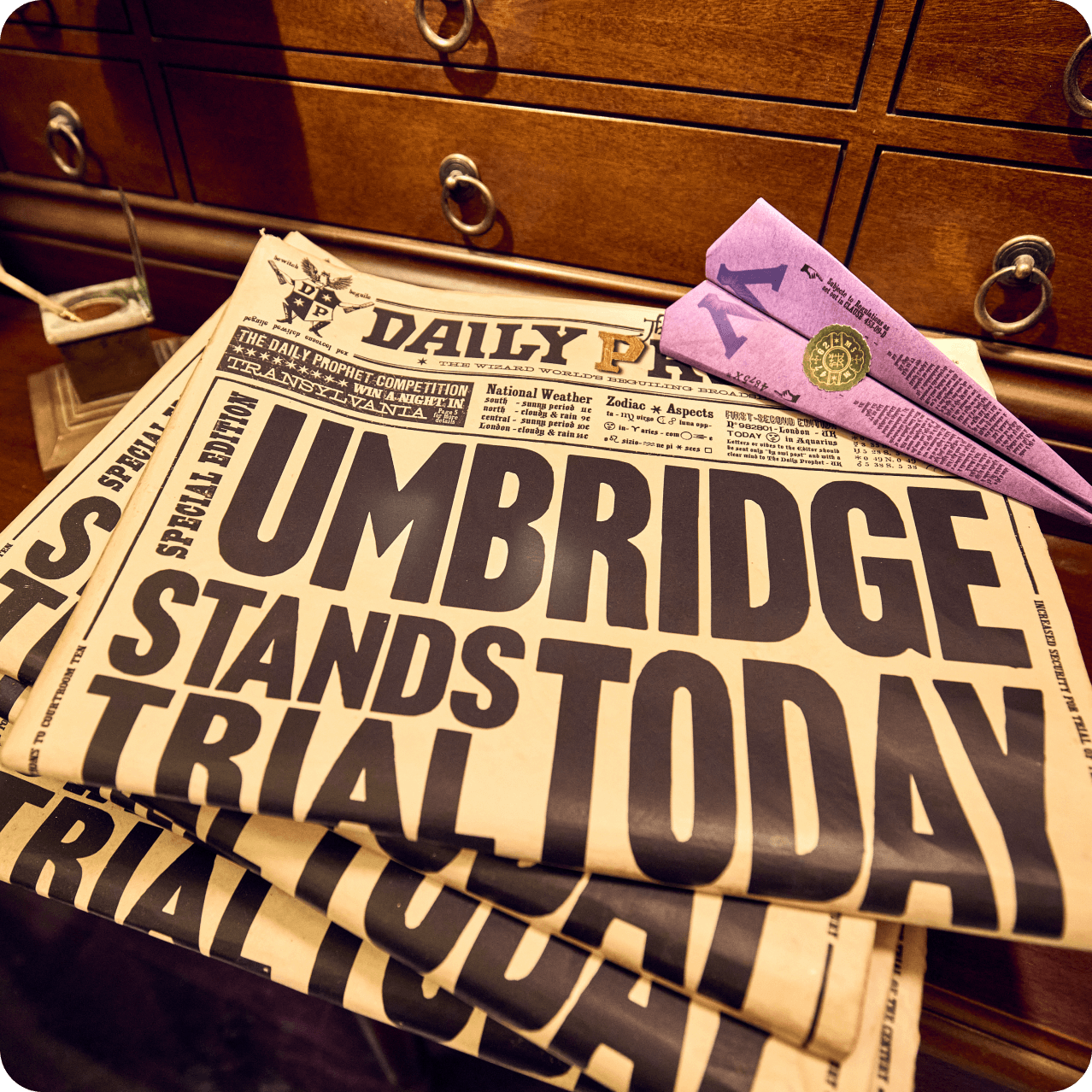 A stack of Daily Prophet newspapers on a desk headlined, "Umbridge Stands Trial Today".