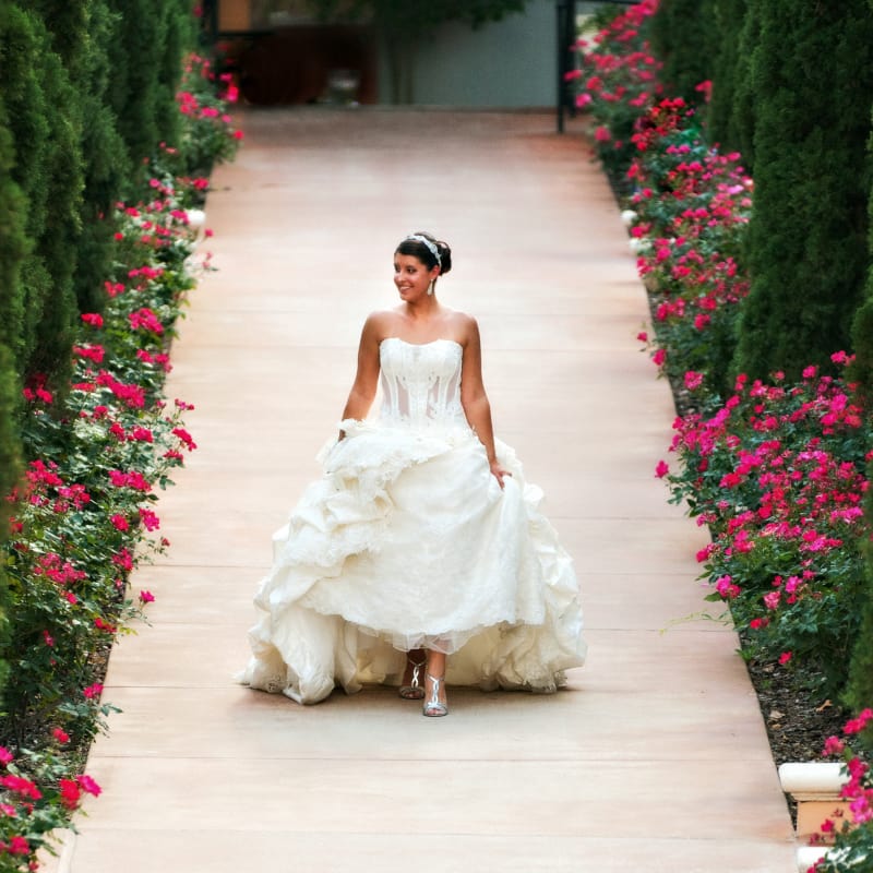 Bride walking down pathway with foliage on both sides.