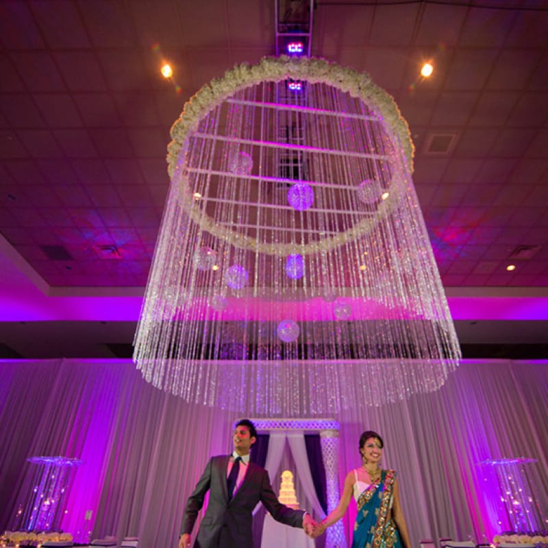 A bride and groom walking below a crystal fixture hanging from a ceiling.