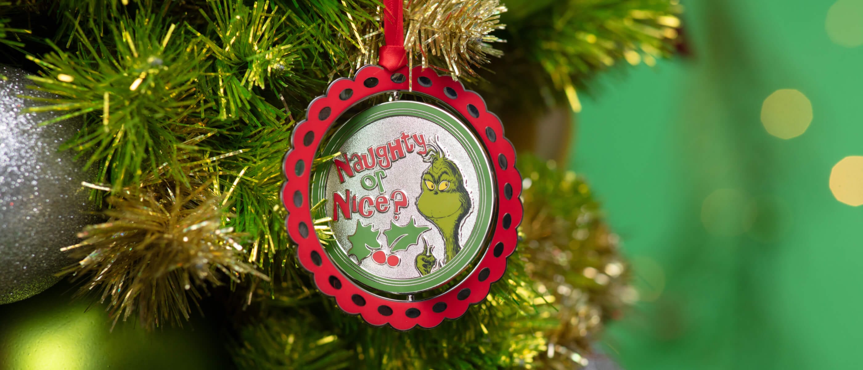 A red and green Christmas tree ornament with the words "Naughty or Nice?" next to the Grinch.