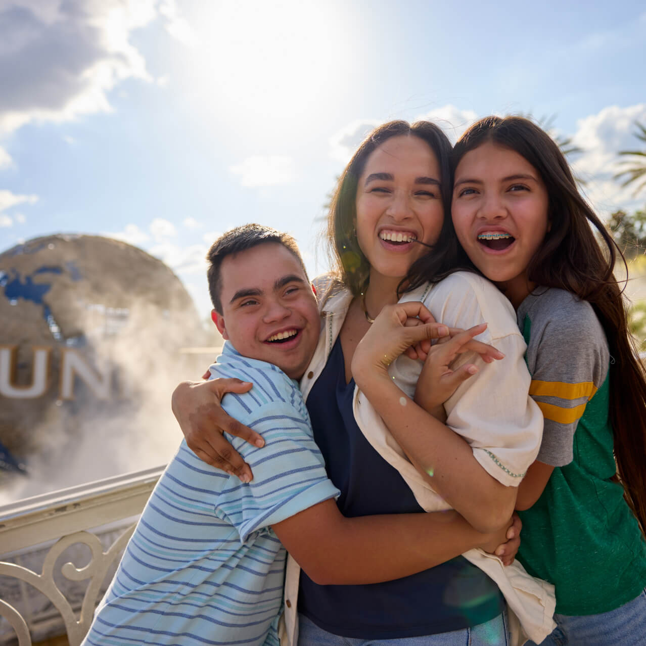 A family of three smiling and embracing as they pose for a photo together in front of the iconic Universal globe.