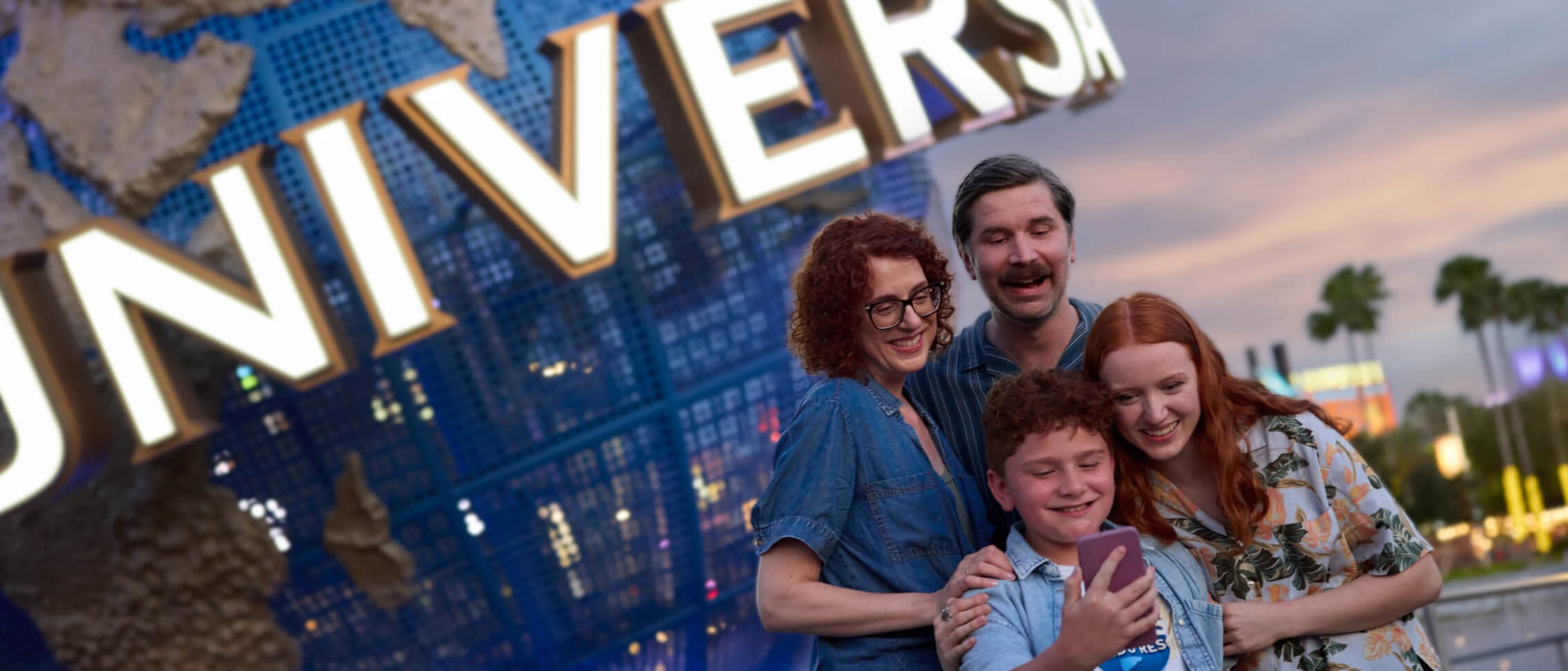 A family of four smiling excitedly as they pose for a selfie together in front of the iconic Universal globe.