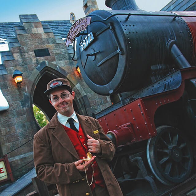 A conductor stands in front of the Hogwarts Express™ in The Wizarding World of Harry Potter™ - Hogsmeade™