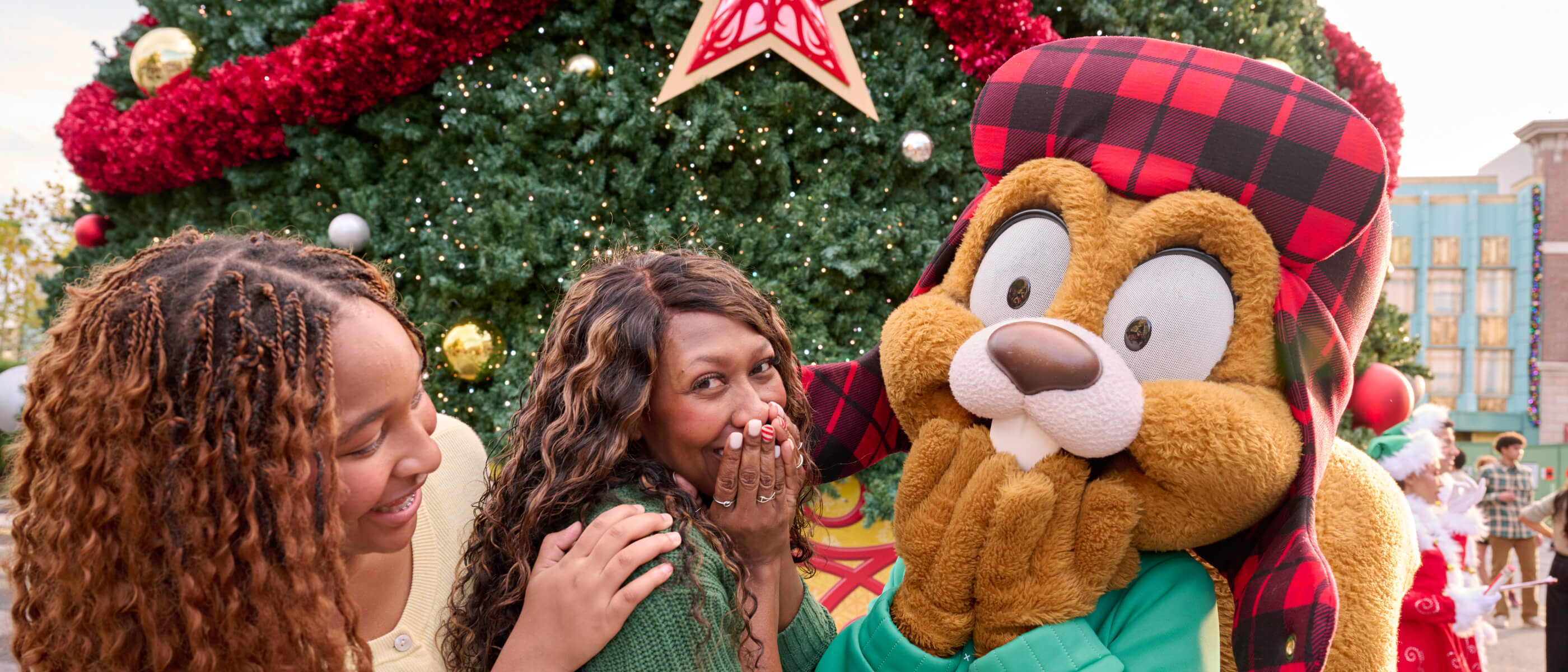 A family smiling and laughing as they pose with Earl the Squirrel in front of festive holiday decorations.
