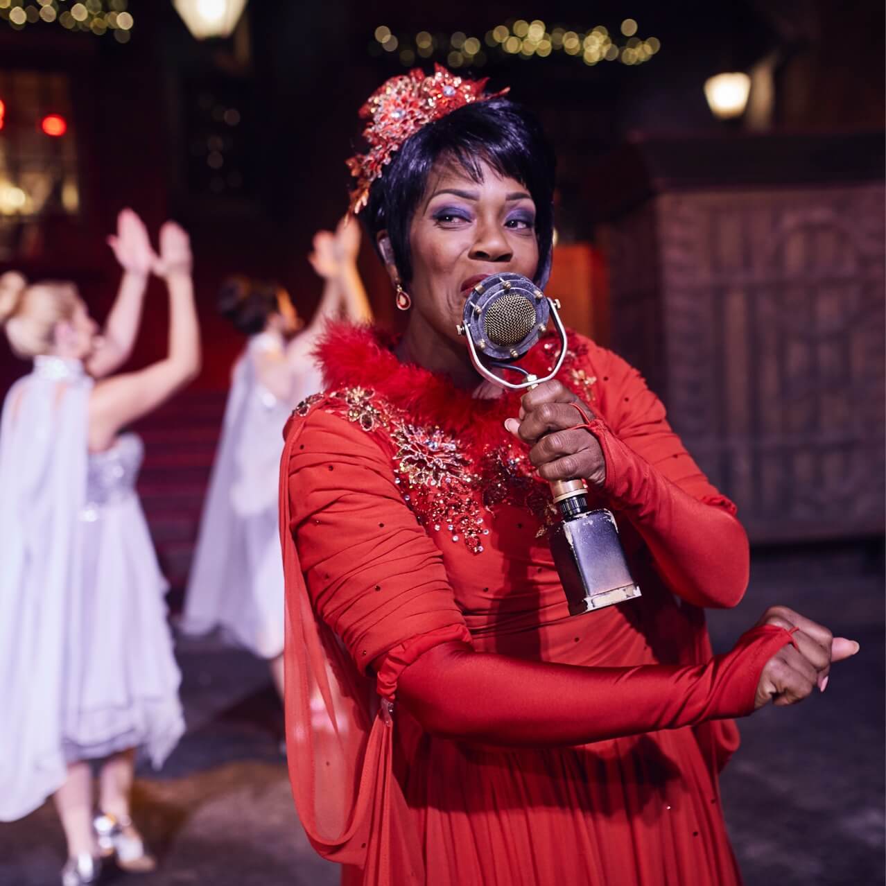 Celestina Warbeck sings in a shimmery red dress with her silvery banshees behind her.