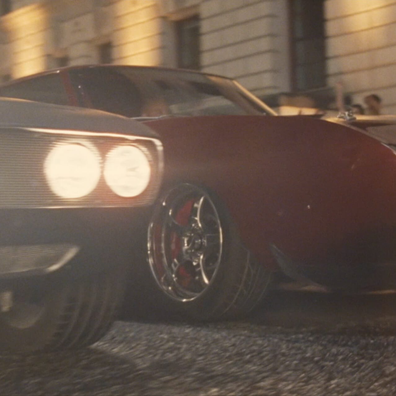 Two cars are side-by-side with their headlights on and are ready to race each other.