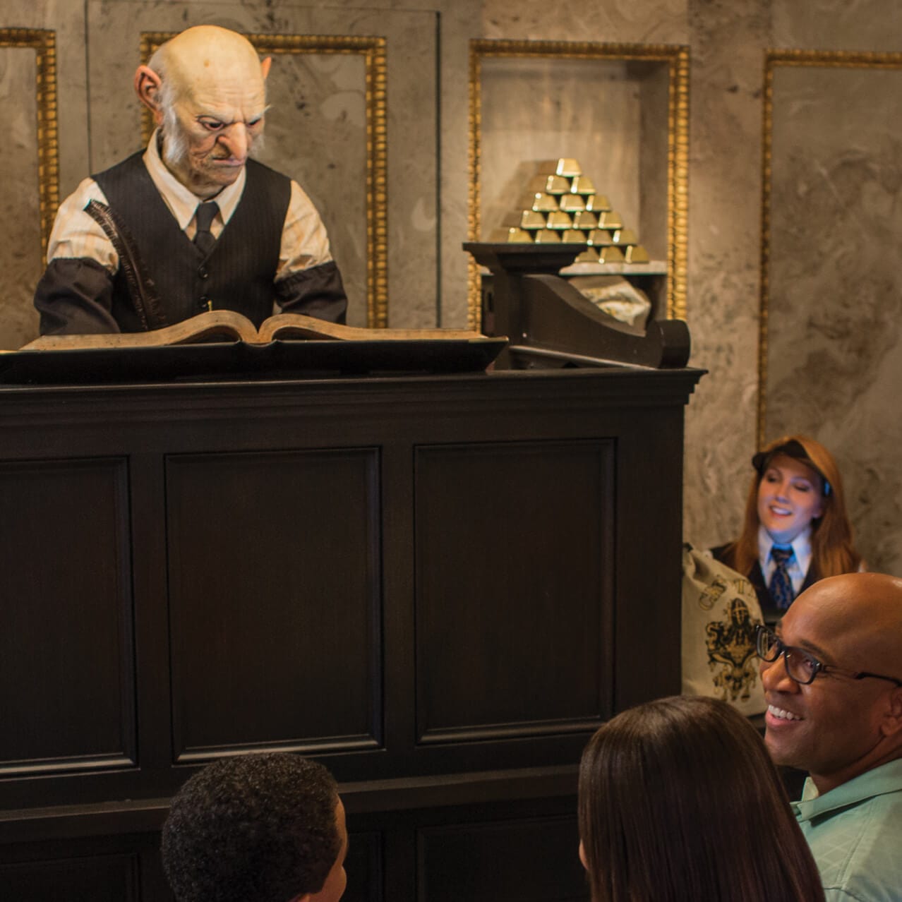 A Gringotts Money Exchange staff member helping Muggle visitors trade their Muggle money for wizarding currency inside Gringott's Money Exchange at The Wizarding World of Harry Potter Diagon Alley at Universal Studios Orlando.