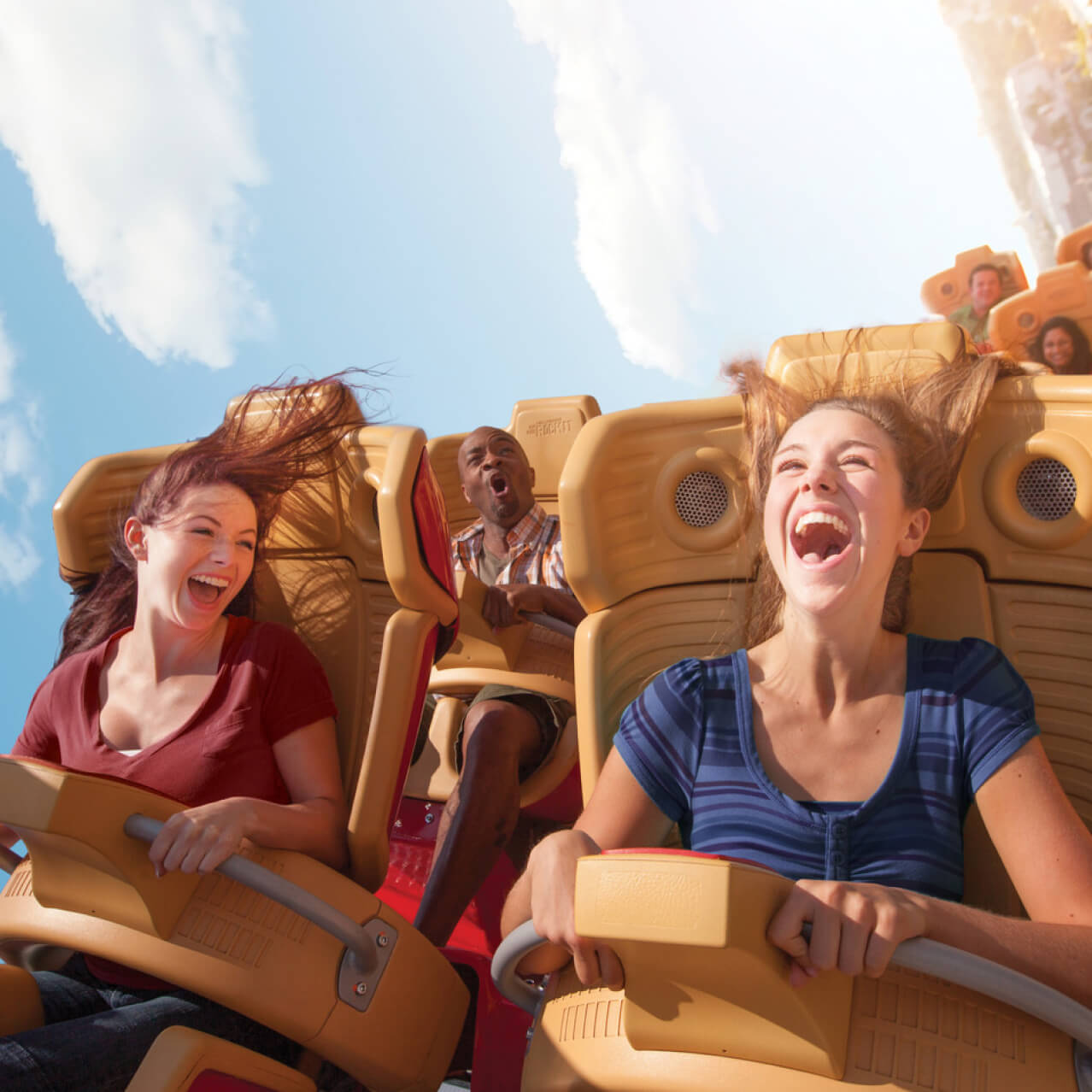 People laughing and screaming on a roller coaster under a bright blue sky.