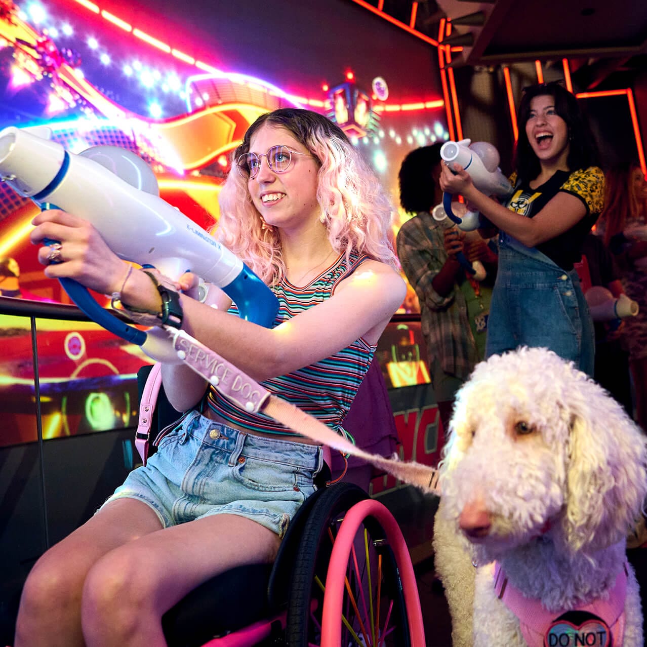 A pair of friends, one with a wheelchair and companion dog, excitedly firing their weapons in Illumination's Villain-Con Minion Blast.