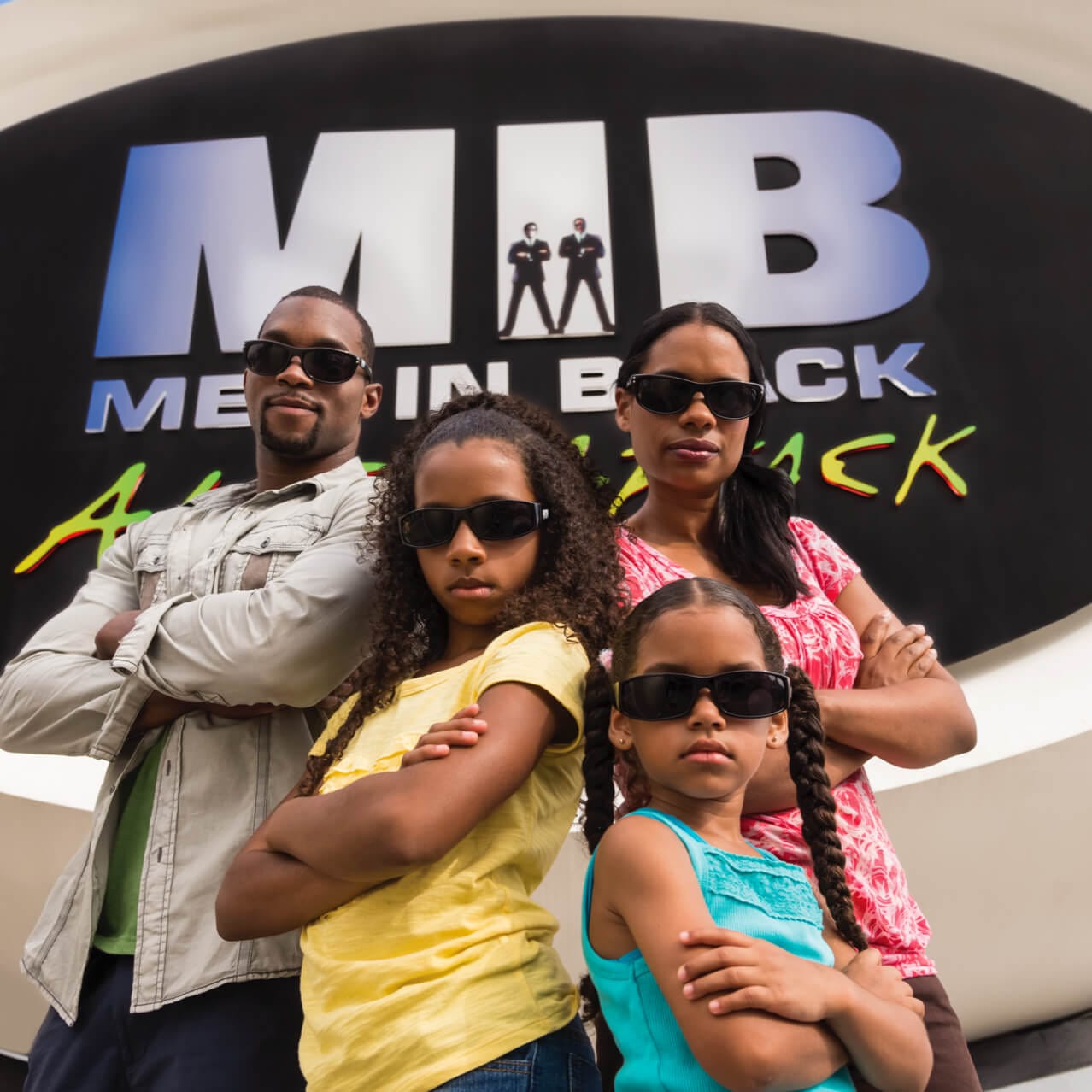 A family wearing sunglasses poses in front of a sign for Men in Black Alien Attack, a competitive laser ride at Universal Studios Orlando.