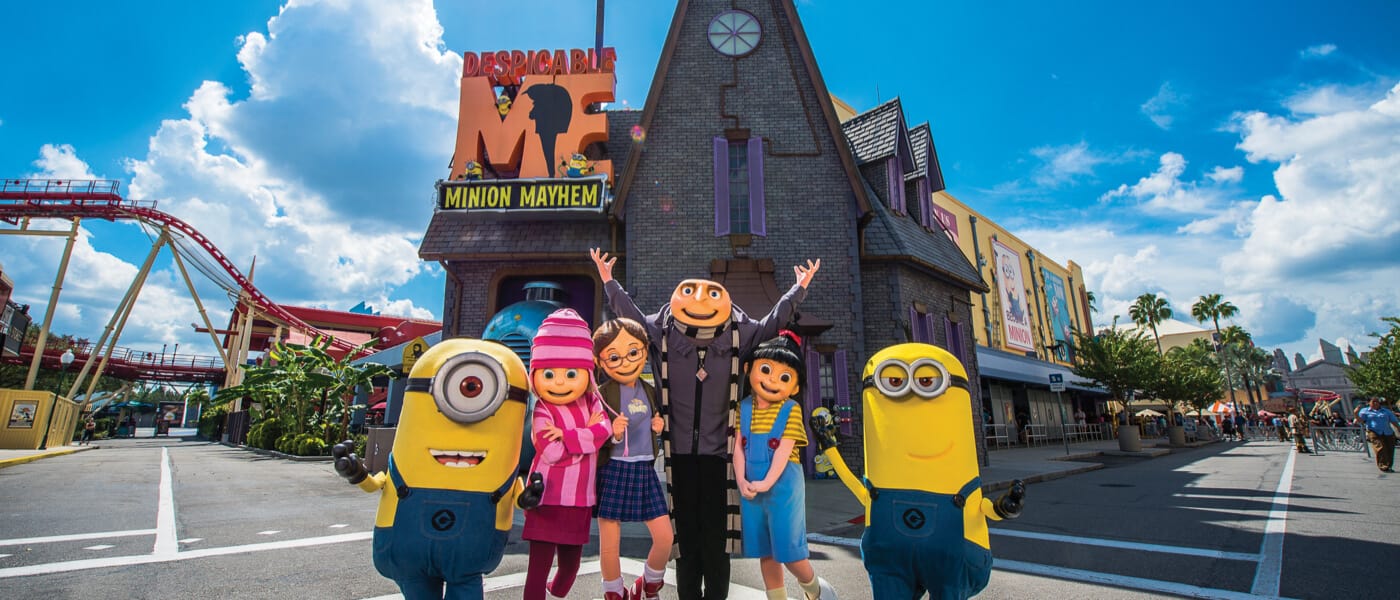 The film characters Gru, his three smiling daughters and two Minions pose in front of the Despicable Me Minion Mayhem attraction.