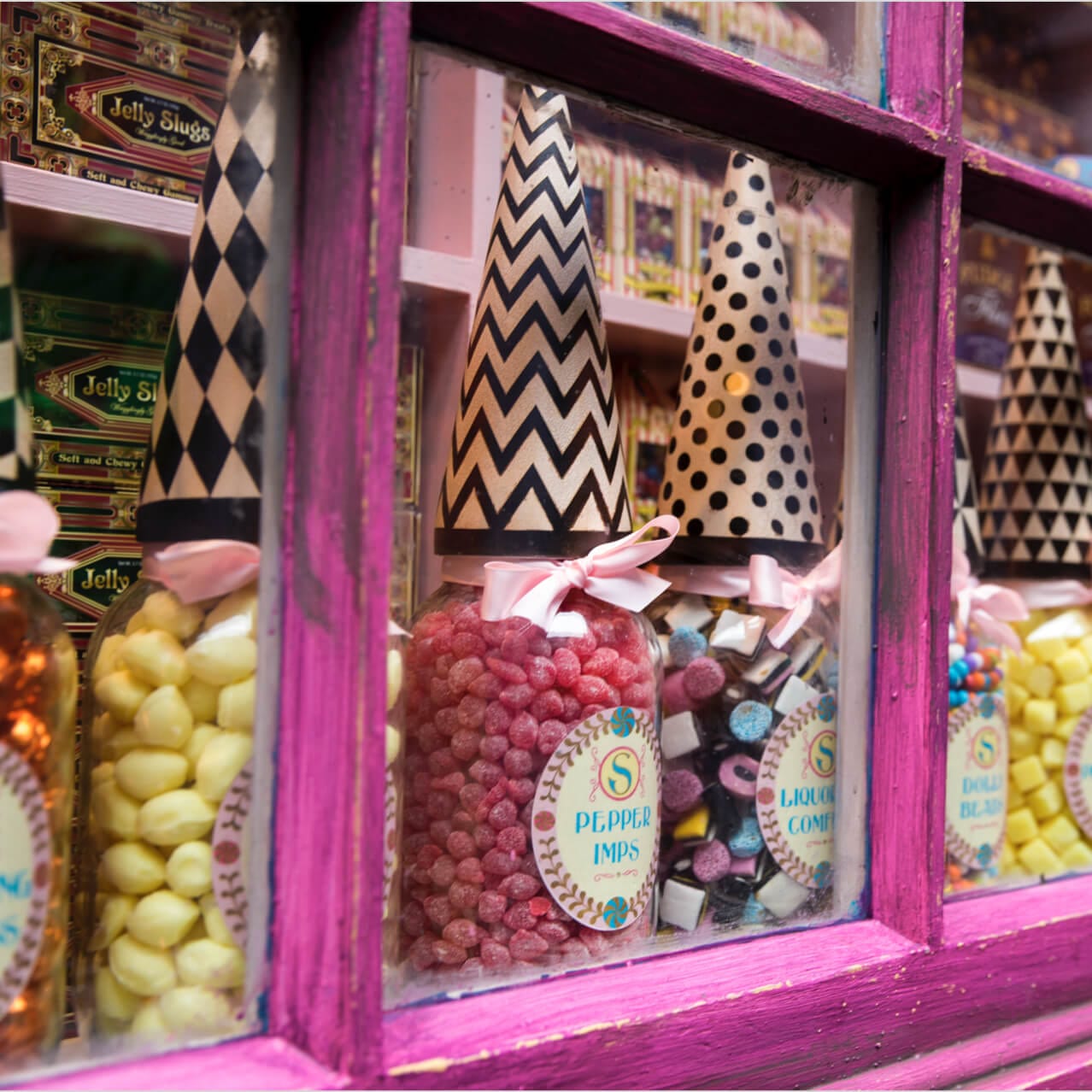 Jars of colourful bulk sweets seen through the pink windows of Sugarplum's Sweet Shop in The Wizarding World of Harry Potter Diagon Alley.