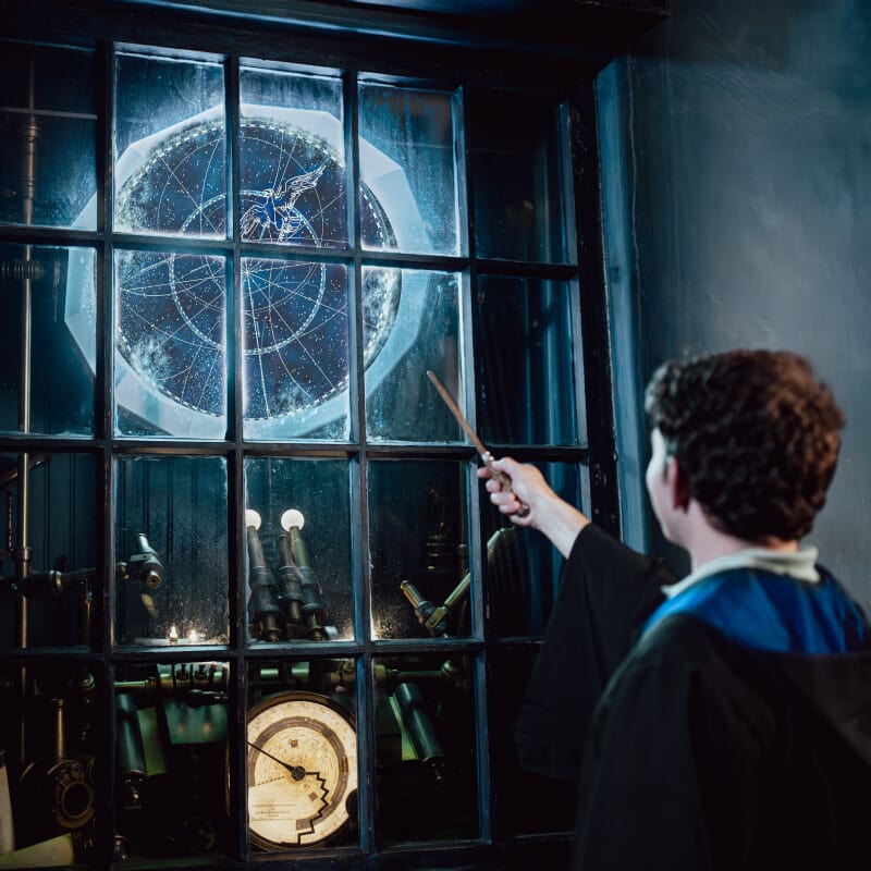 A guest pointing a wand at a shop window where a large multi-sided object hovers and glows.