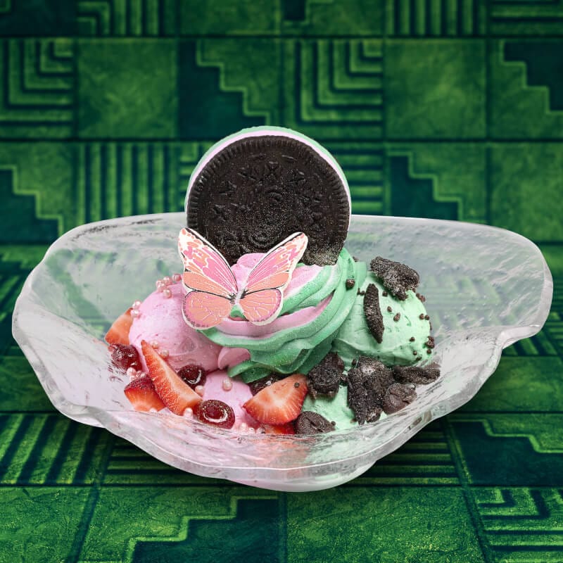 Pink and green ice cream topped with strawberries, cookie crumbles, a cookie sandwich and a pink butterfly