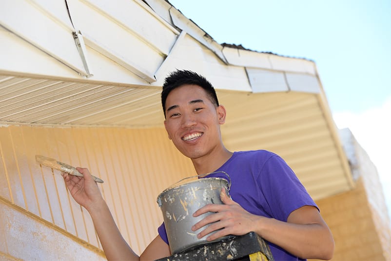 A volunteer wearing a purple t-shirt, holding a paint can and painting.