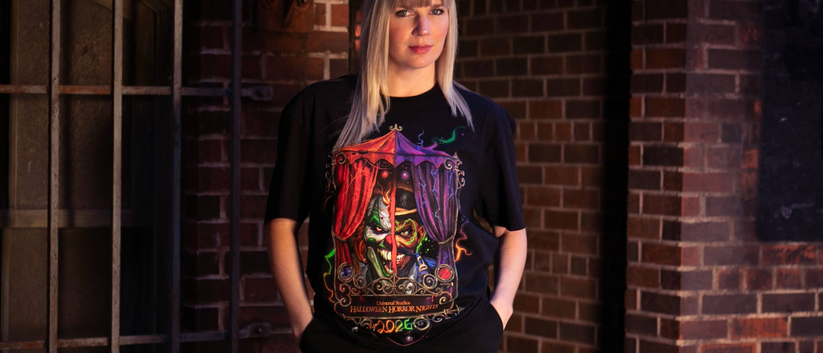 A Guest in a dim brick alley wearing a black “Universal Studios HALLOWEEN HORROR NIGHTS 2026” Jack and Dr. Oddfellow T-shirt.