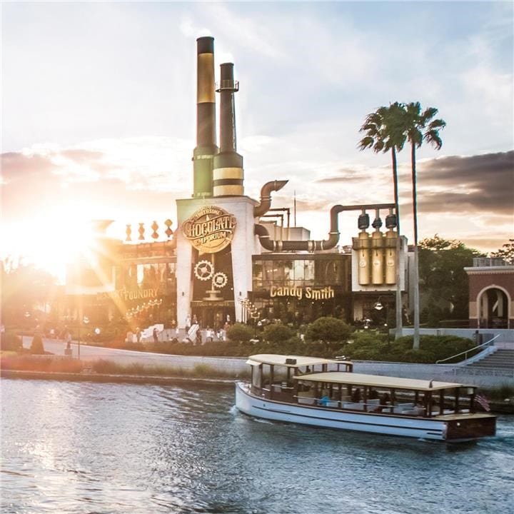 Universal Orlando's CityWalk lagoon with a water taxi carrying passengers to the hotels and the Islands of Adventure entrance tower in the background.