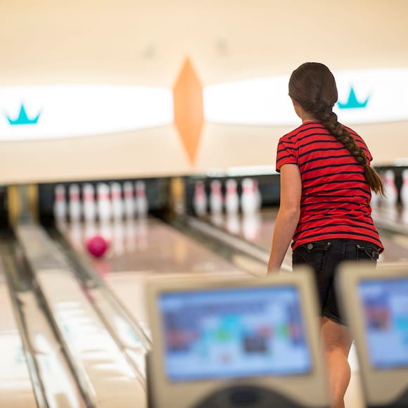 A girl in a red and black striped shirt watches as her bowling ball rolls down the lane at Universal Orlando's Galaxy Bowl.