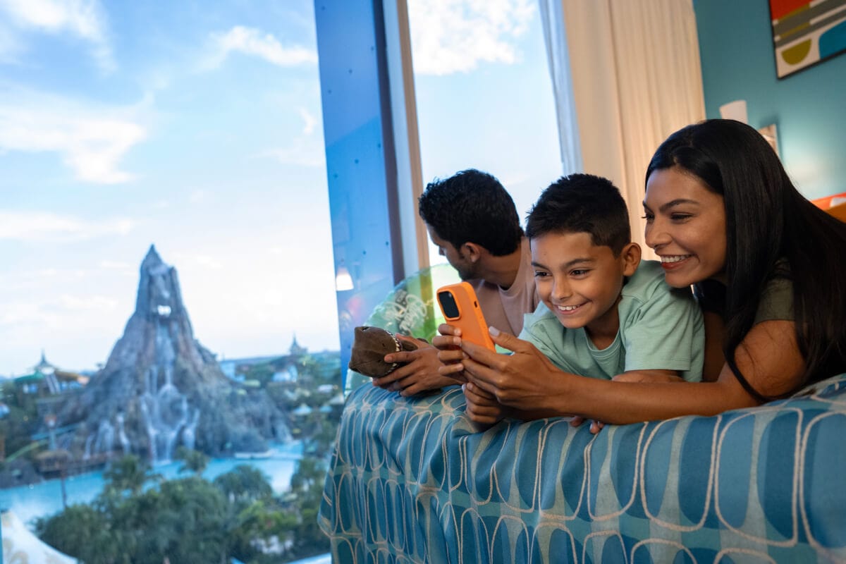 A happy family of three relaxing in their hotel room at Cabana Bay Beach Resort overlooking Volcano Bay.