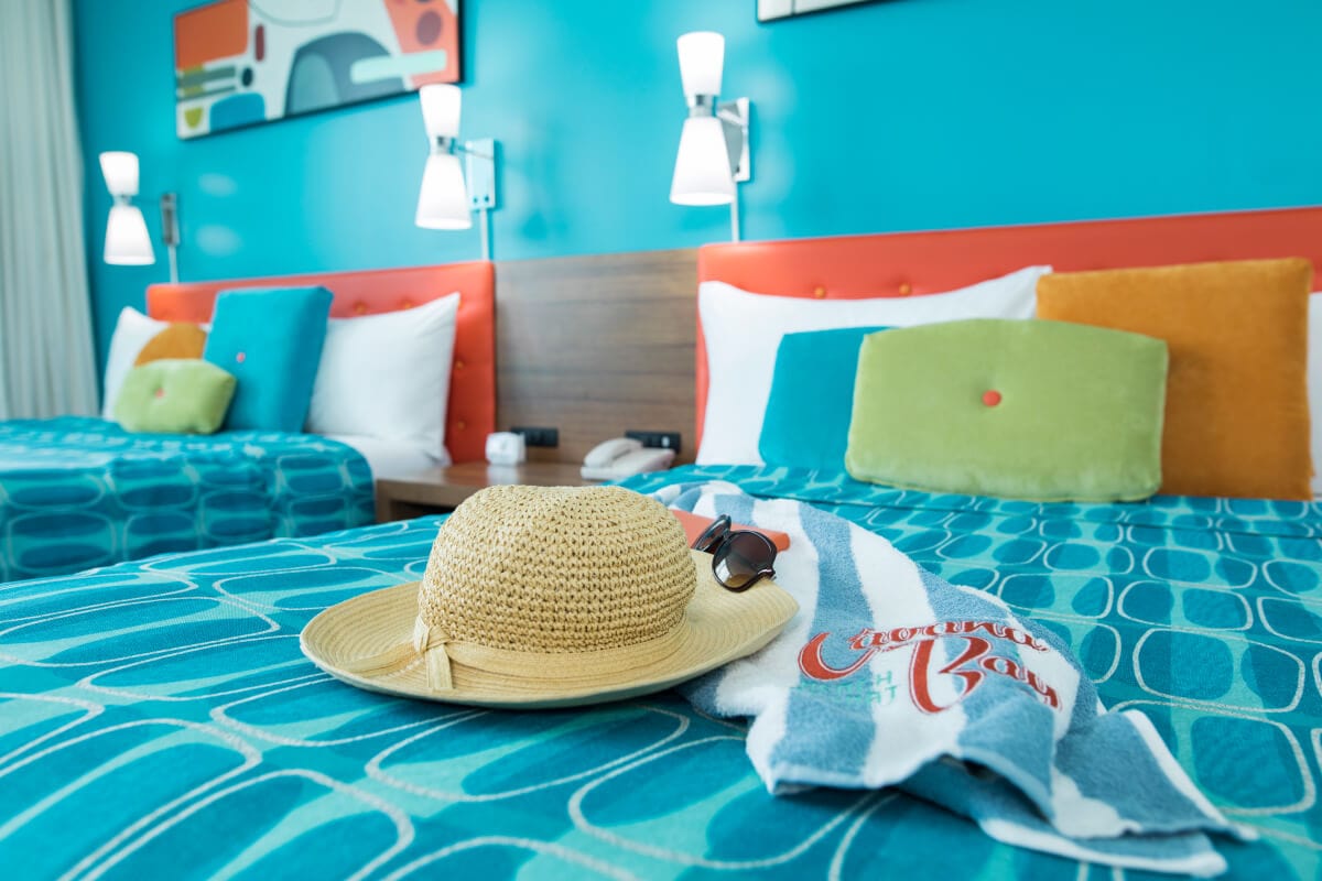 A sunhat, glasses, and branded towel on a queen bed at Universal Cabana Bay Beach Resort